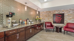 A modern kitchen with a coffee machine, a sink, and a countertop with various items. There are two red chairs and a small table. A sign on the wall reads "Red Roof Inn." - Red Roof Inn Baton Rouge (Baton Rouge)