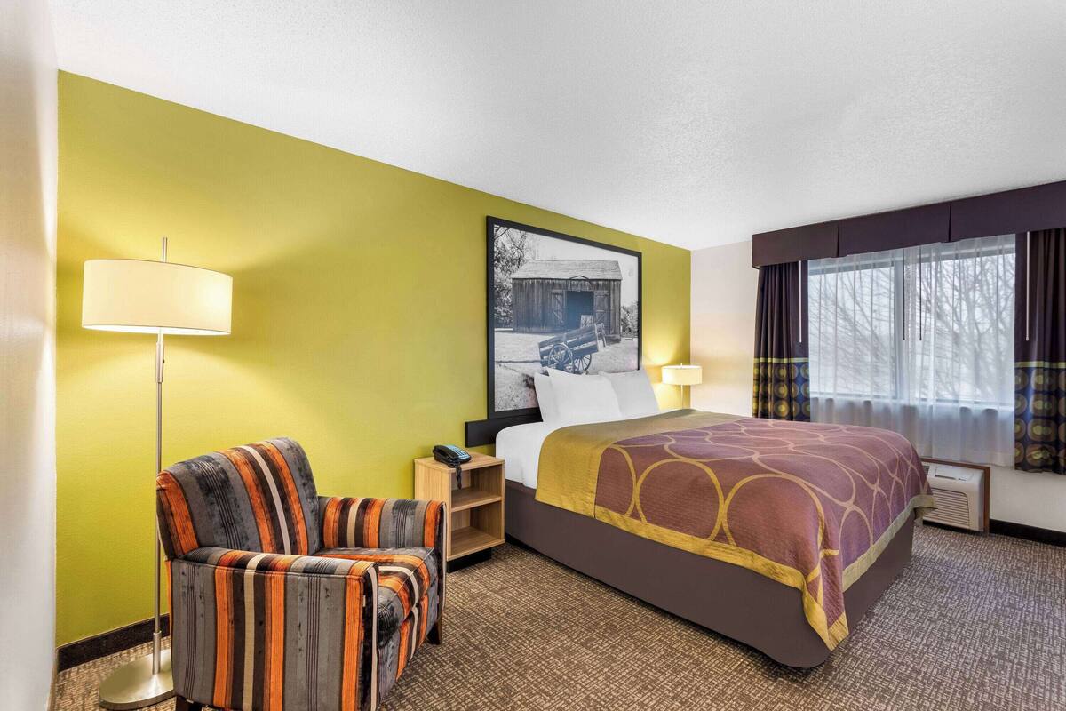 A hotel room with a bed, a chair, a lamp, a picture on the wall, and a window with curtains.