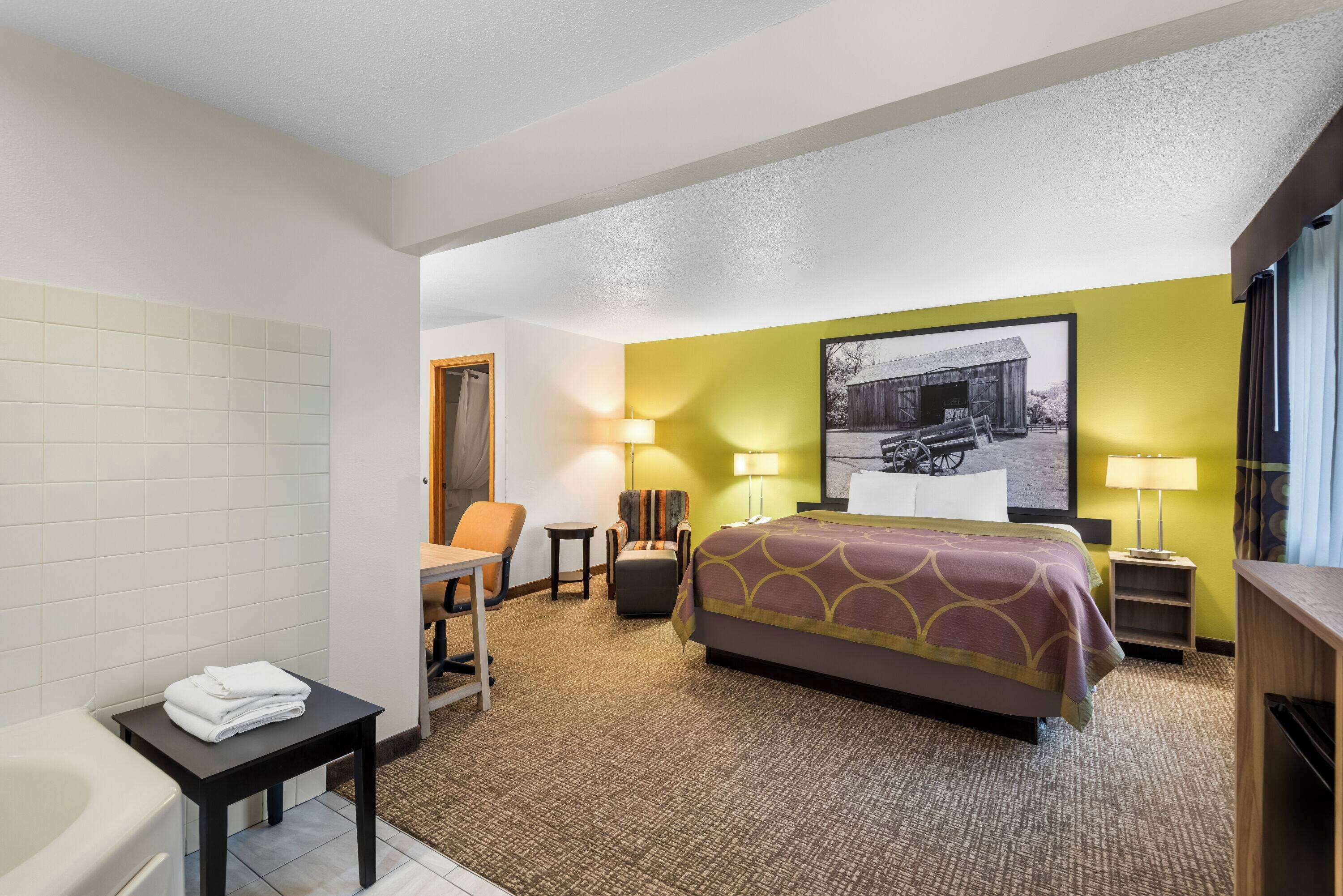 A hotel room with a bed, a chair, a small table, a lamp, and a picture on the wall.