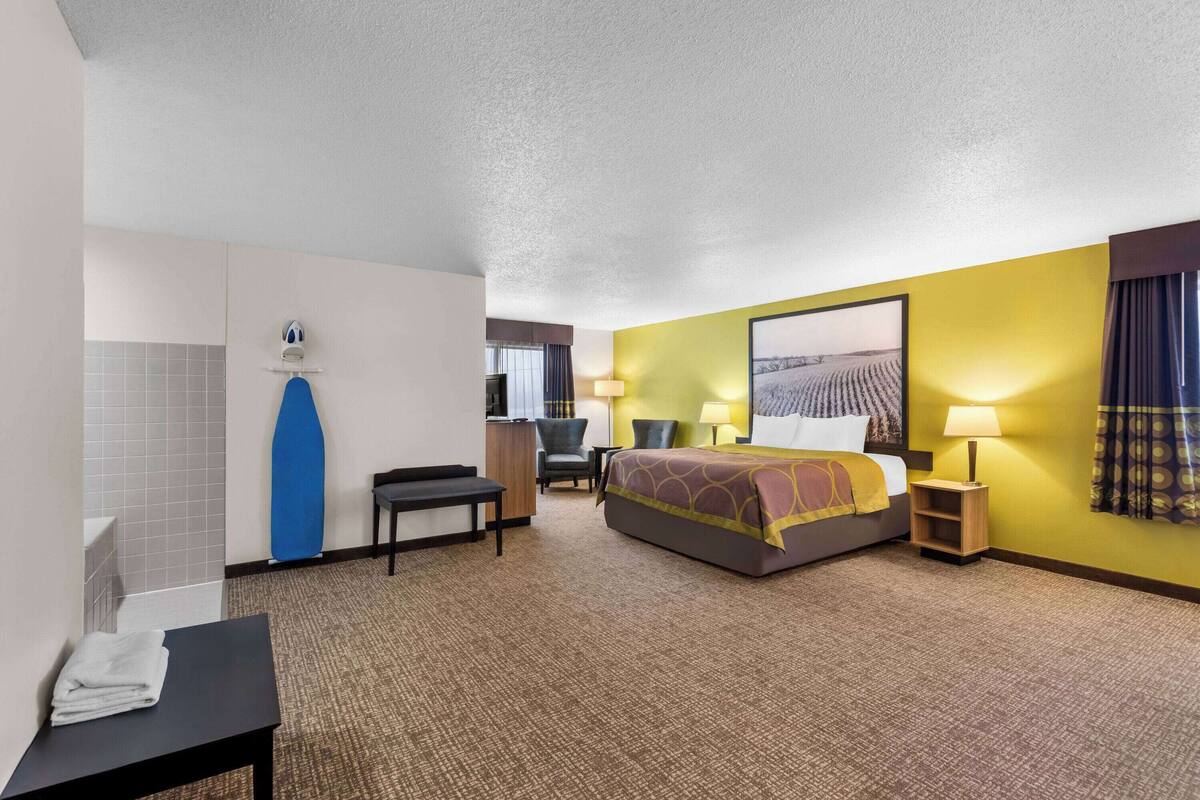A hotel room with a bed, a desk, a chair, a bathroom, and a large window.