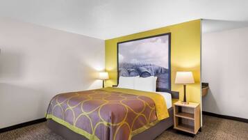 A hotel room with a bed, a nightstand with a lamp, and a wall-mounted painting.
