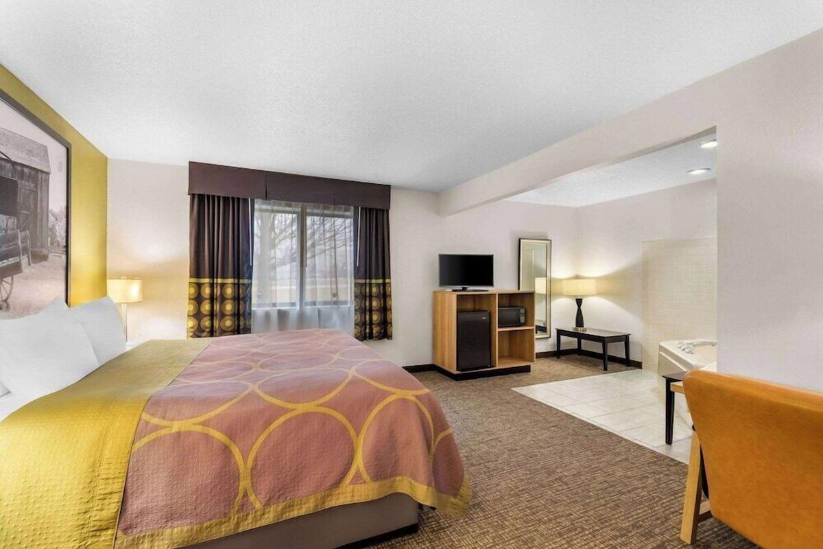 A hotel room with a bed, a TV, a desk, a chair, and a window with curtains.