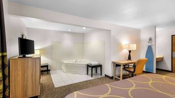Habitación de hotel con cama, escritorio, silla, televisor, bañera y una mesita.