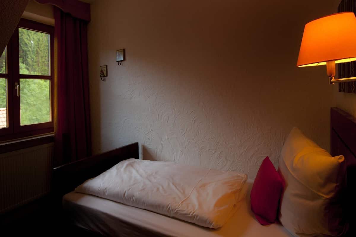 A bedroom with a bed, a window, a wall-mounted lamp, and a radiator.