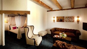 Un dormitorio con cama con dosel, una chaise lounge, un sofá y una mesita con una botella y flores.