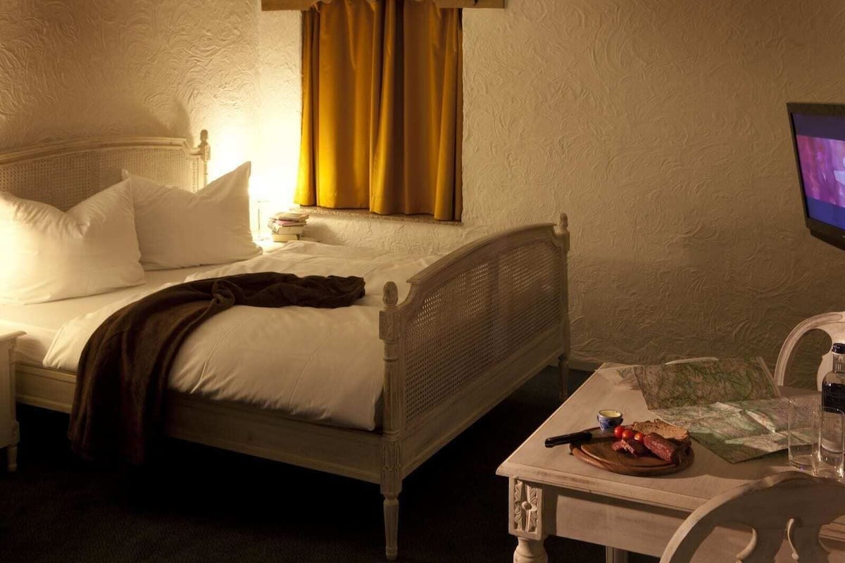 A hotel room with a bed, a table with a map, a bottle, and a glass.