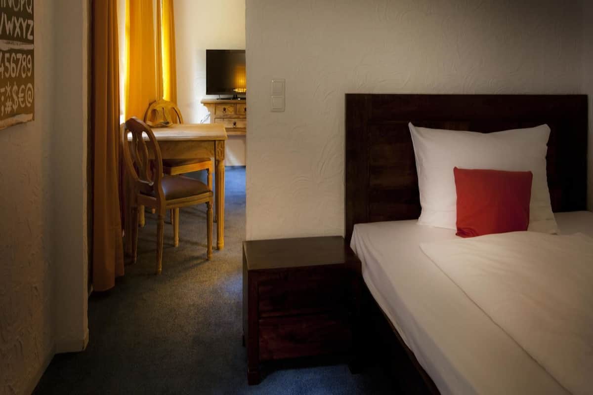 A hotel room with a bed, a desk with a chair, a television, and a small table.