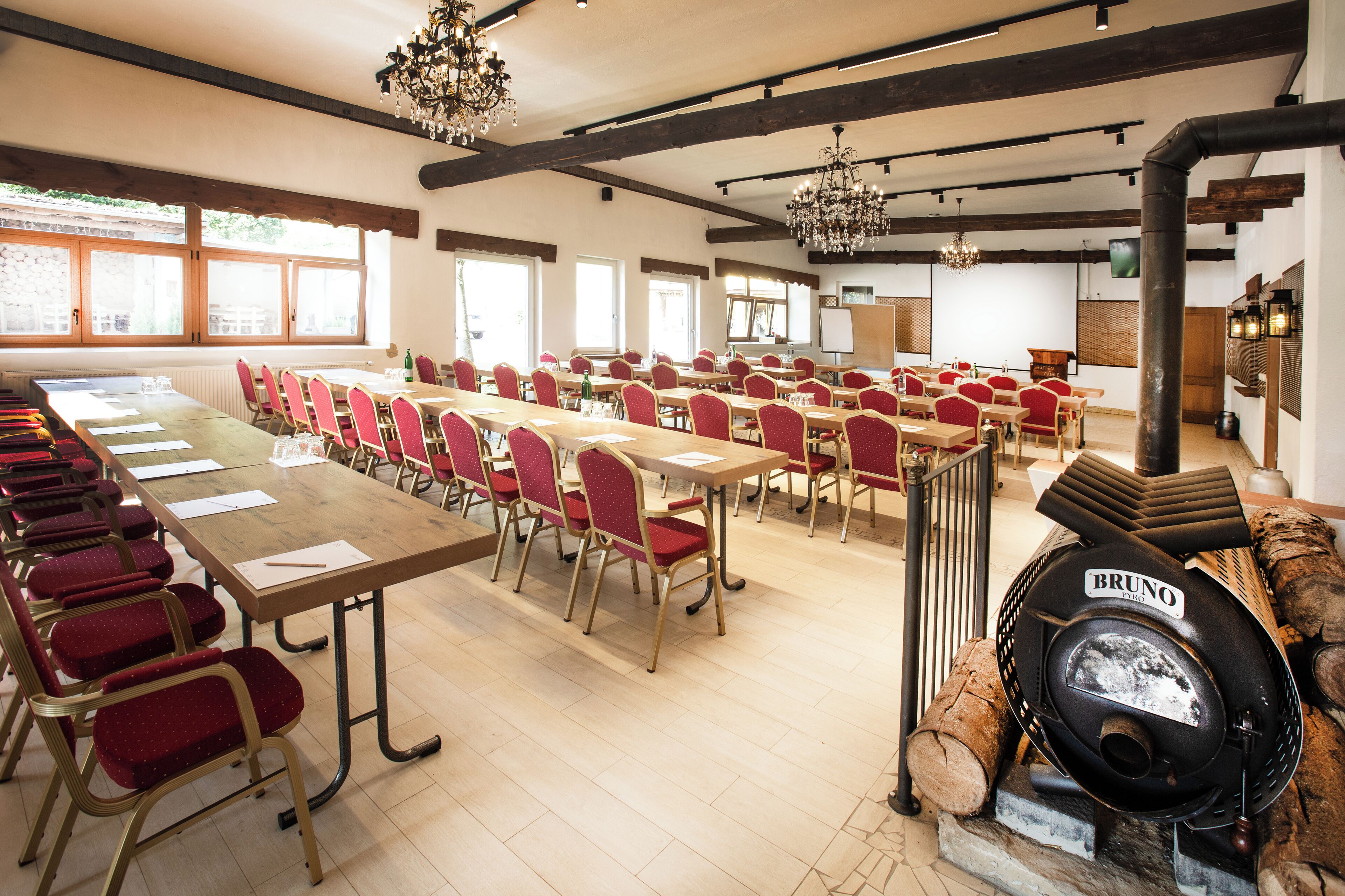 Un salón de conferencias con largas mesas y sillas rojas, vigas de madera y candelabros.