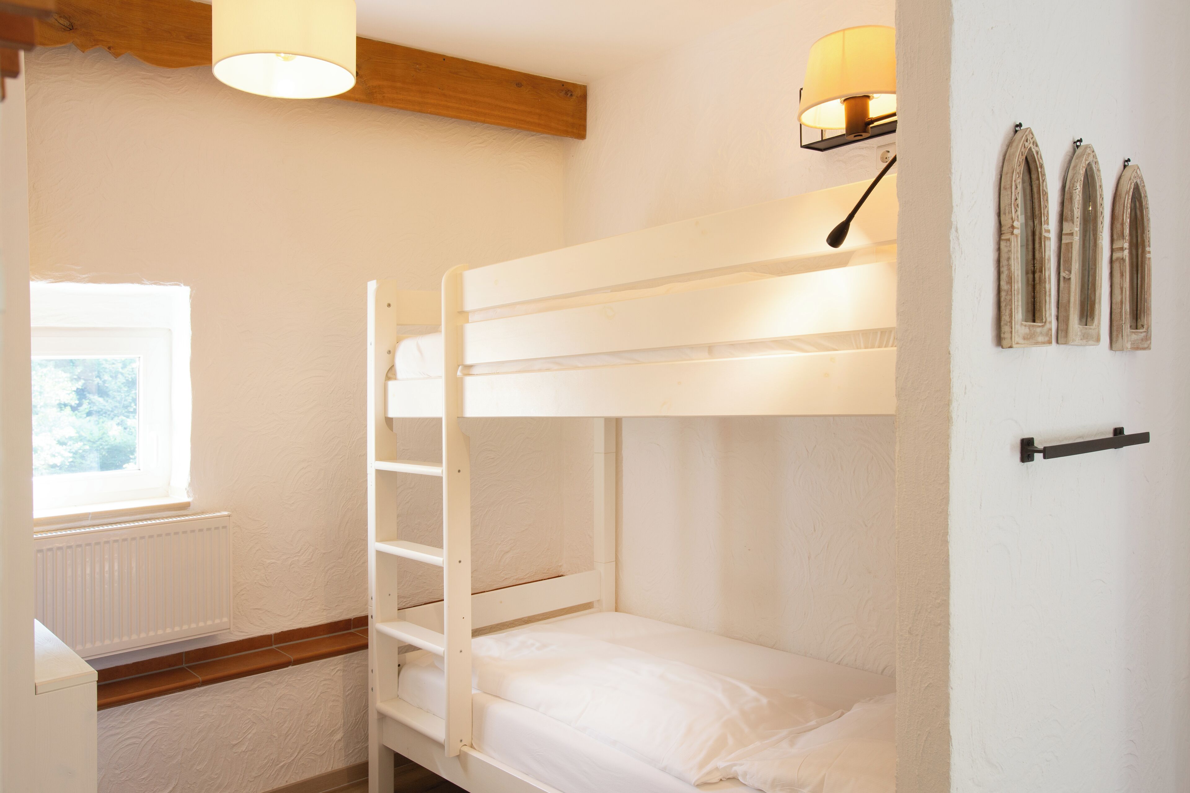 A bunk bed room with a window, a radiator, and wall-mounted lamps.