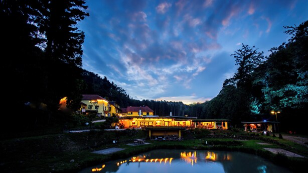 Un hotel junto al lago con su reflejo en el agua, rodeado de árboles y un cielo despejado.