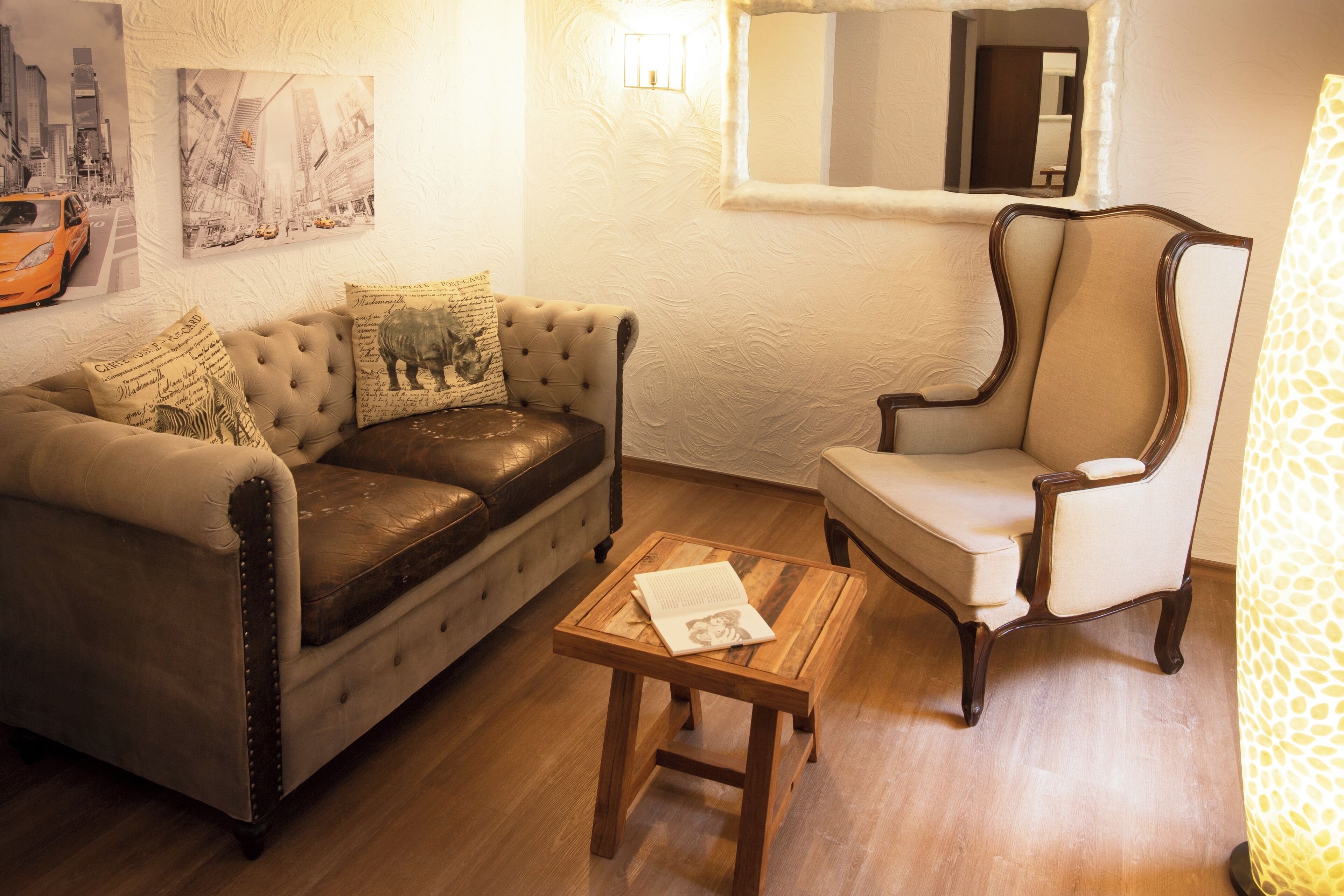 Un salon avec un canapé en cuir, une table basse en bois, un fauteuil blanc et un miroir au mur.
