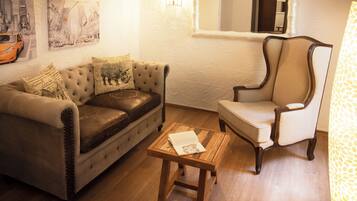 Un salon avec un canapé en cuir, une table basse en bois, un fauteuil blanc et un miroir au mur.