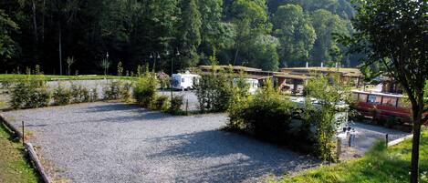 A gravel parking area with RVs and a bus, surrounded by trees and a mountain in the background.