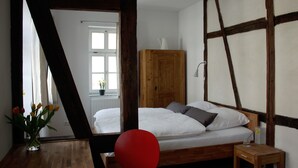 A bedroom with a wooden bed, a red chair, a wooden cabinet, and a window with a view of a white building. - Pension Sackpfeifenmühle (Erfurt)