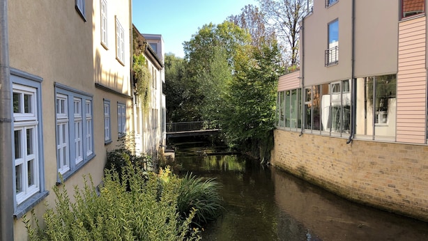 A narrow canal flanked by buildings with large windows and a bridge in the background. - Pension Sackpfeifenmühle (Erfurt)