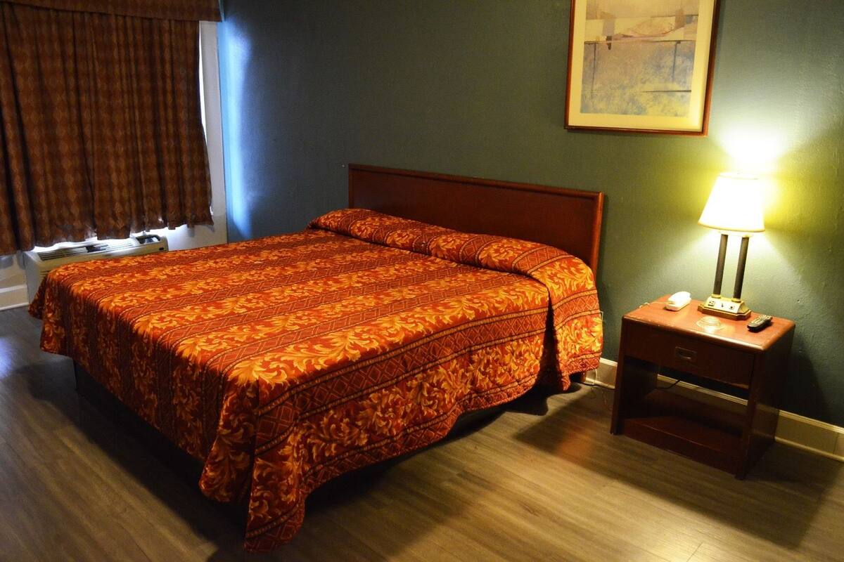A hotel room with a bed, a nightstand with a lamp, and a painting on the wall.