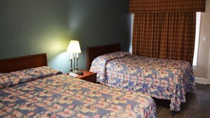 A hotel room with two beds, a nightstand with a lamp, and a window with curtains.