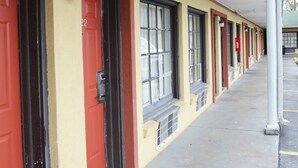 A row of motel rooms with red doors and windows, a covered walkway, and a parking lot.