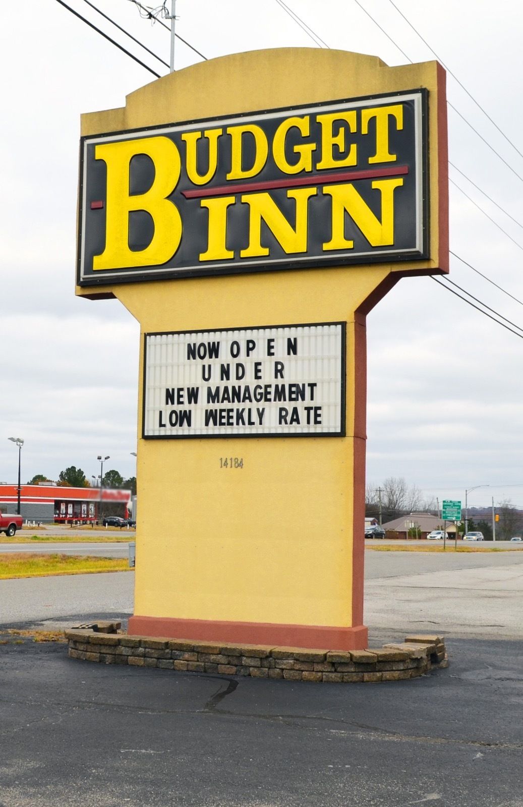 A sign for Budget Inn stating it is now open under new management with a low weekly rate.