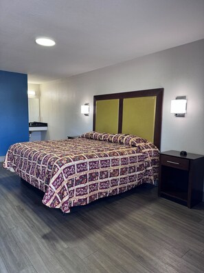 A hotel room with a bed, bedside table, nightstand, and a mirror. - Budget inn (Russellville)