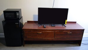 A wooden desk with a flat-screen TV, a remote control, and a microwave on top.