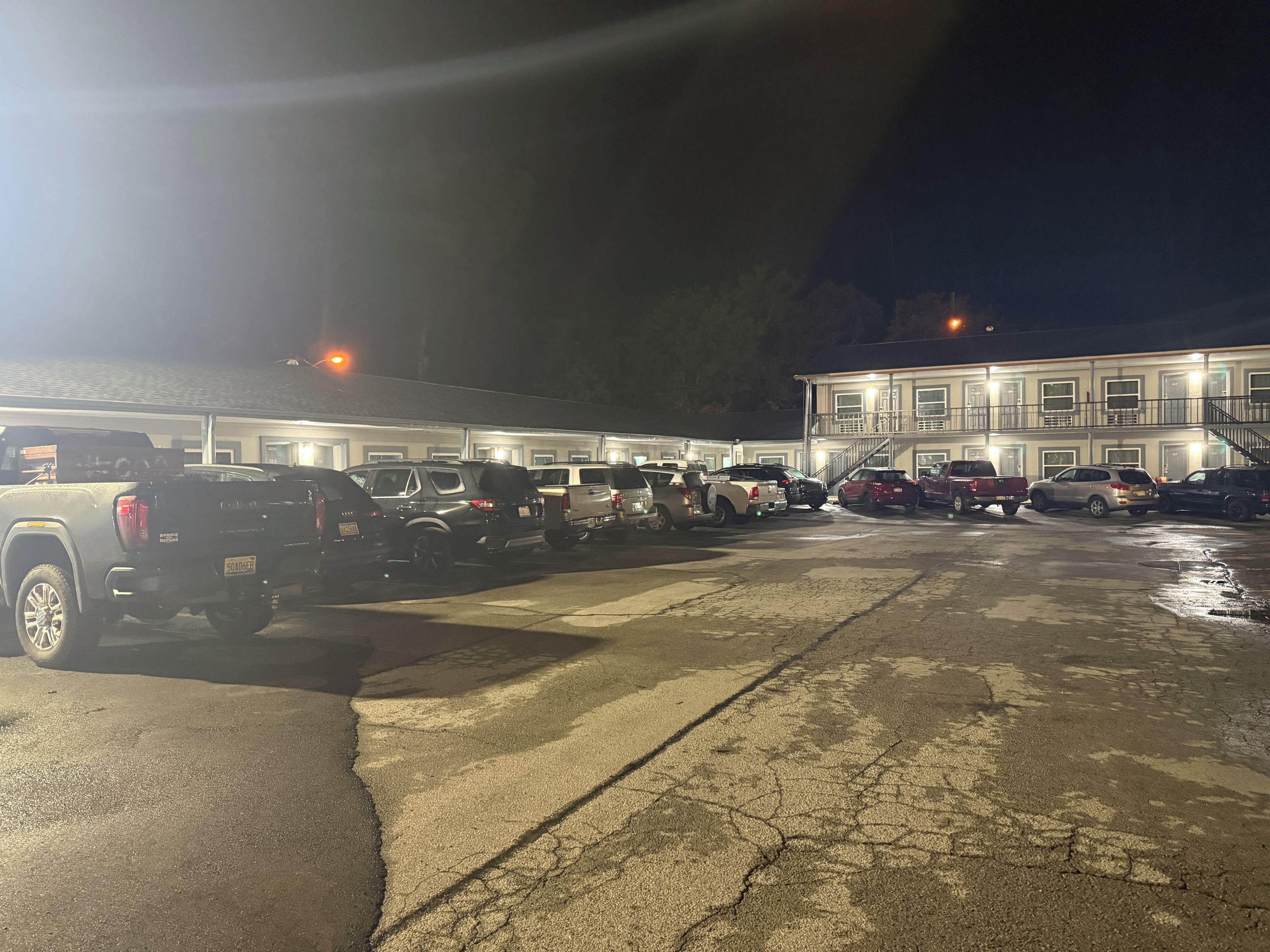 A parking lot with multiple vehicles and a building with multiple doors and windows.