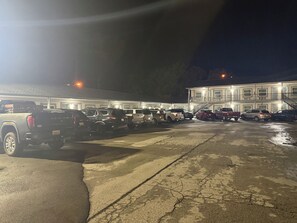 A parking lot with multiple vehicles and a building with multiple doors and windows. - Budget inn (Russellville)