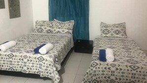 A room with two beds, each with patterned bedding and pillows, a blue curtain, and a small black object on the floor. - Casa Bella San Andres (San Andrés)