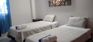 A hotel room with two single beds, each with a pillow and a rolled towel.
