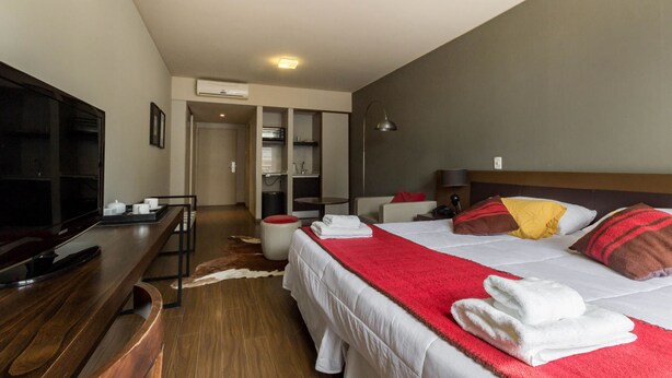 Een moderne hotelkamer met een groot bed, een flatscreen televisie, een houten bureau en een zithoek met een stoel en een klein tafeltje.