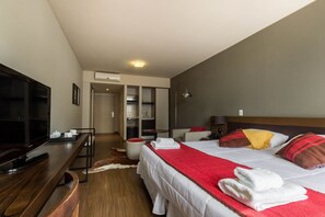 Une chambre d’hôtel moderne dotée d’un grand lit, d’un téléviseur à écran plat, d’un bureau en bois et d’un coin salon avec une chaise et une petite table.