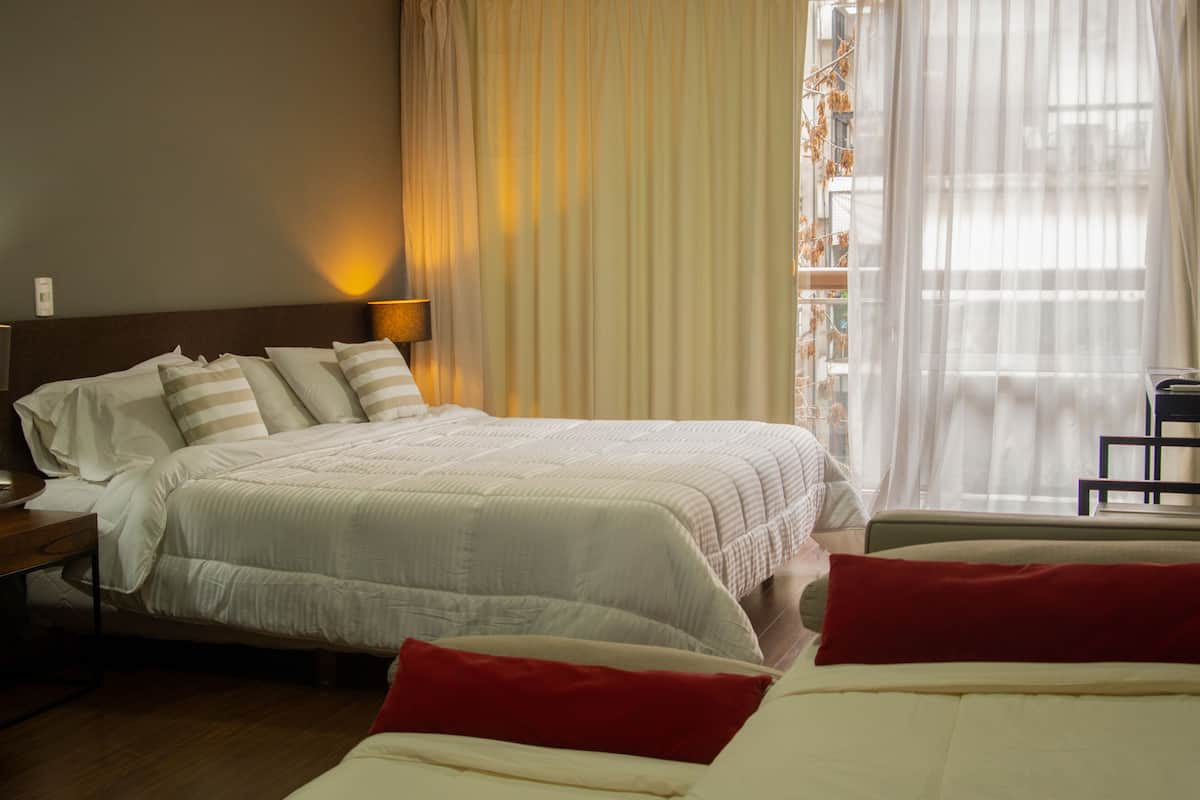 Een hotelkamer met een groot bed, een nachtkastje, een lamp en een raam met gordijnen.
