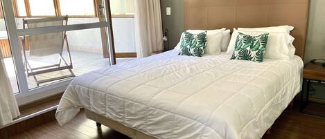A bedroom with a large bed, wooden flooring, a window with curtains, and a view of the outside.