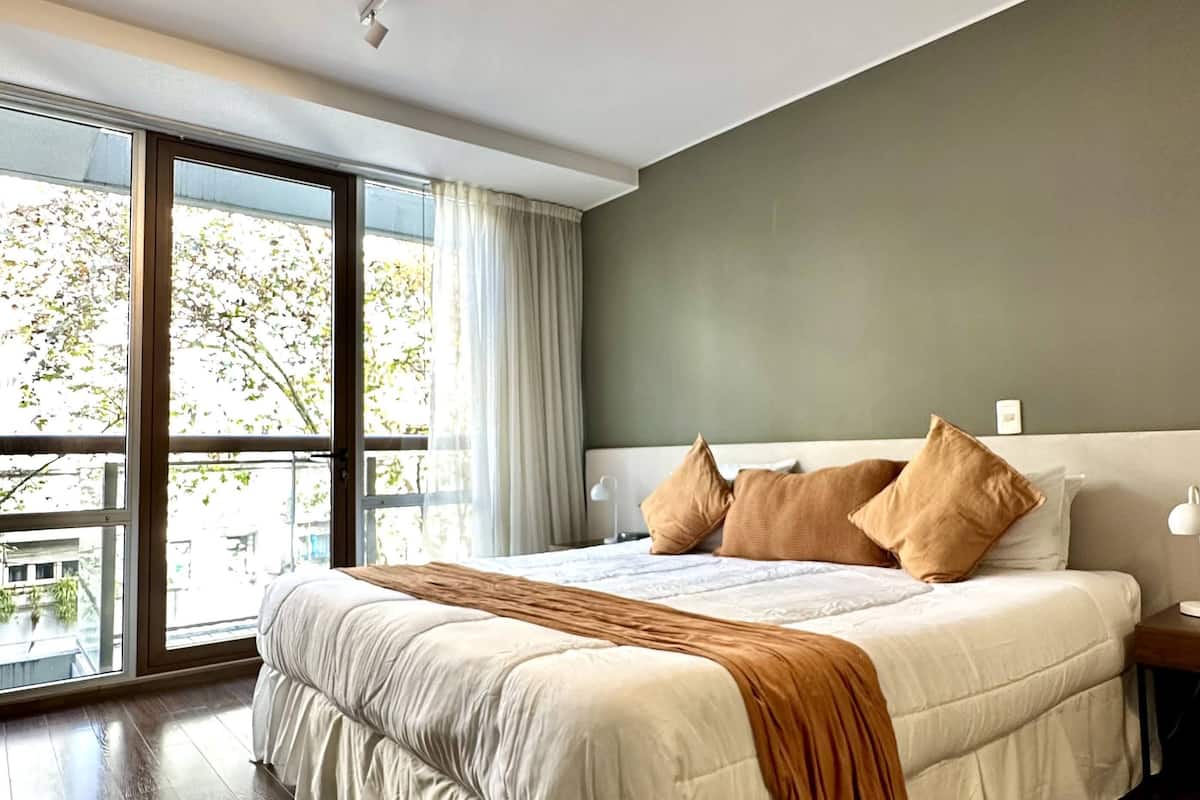 Een ruime slaapkamer met een groot bed, een nachtkastje en uitzicht op een balkon.