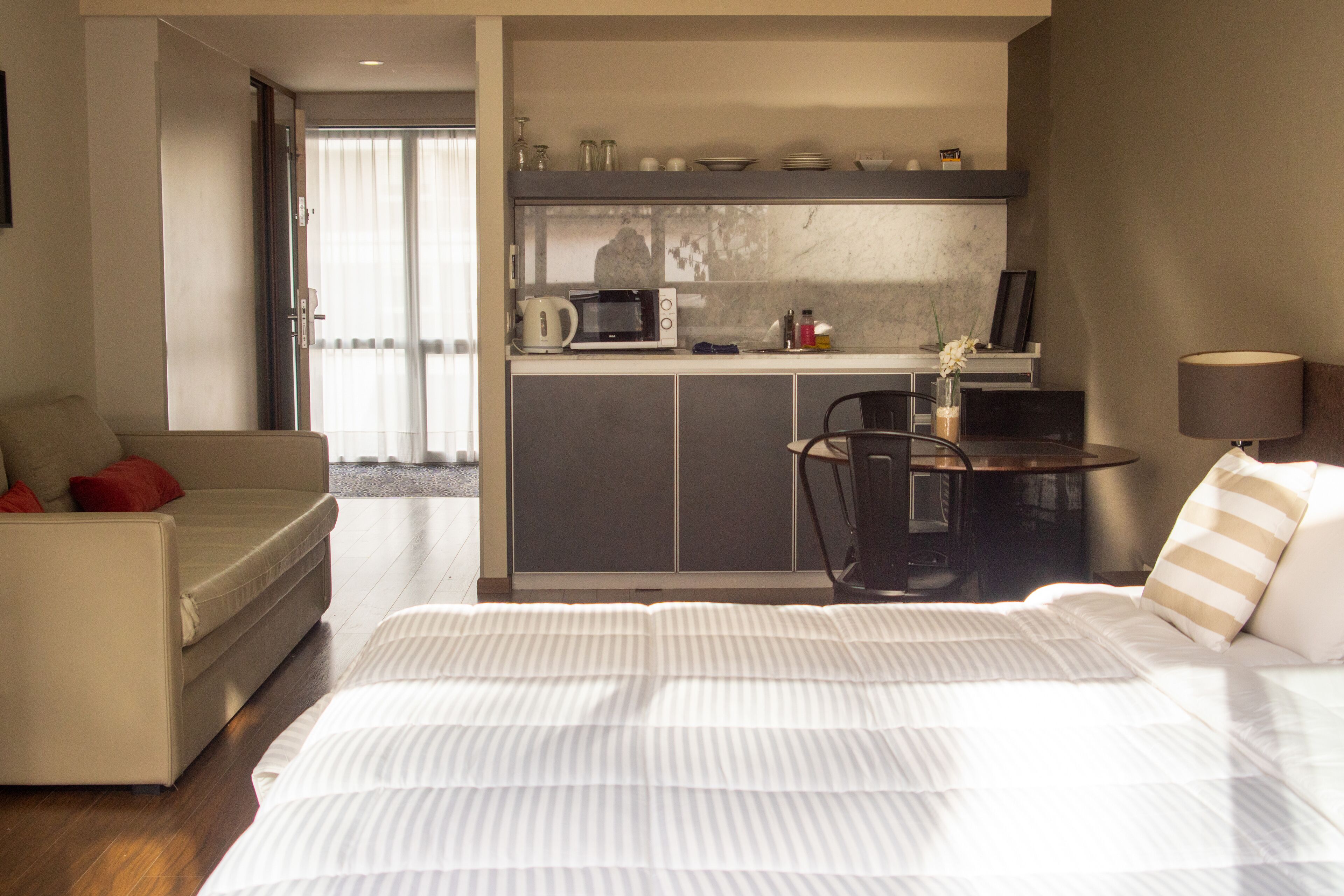 A hotel room with a bed, a sofa, a small kitchenette, and a view of the outside.