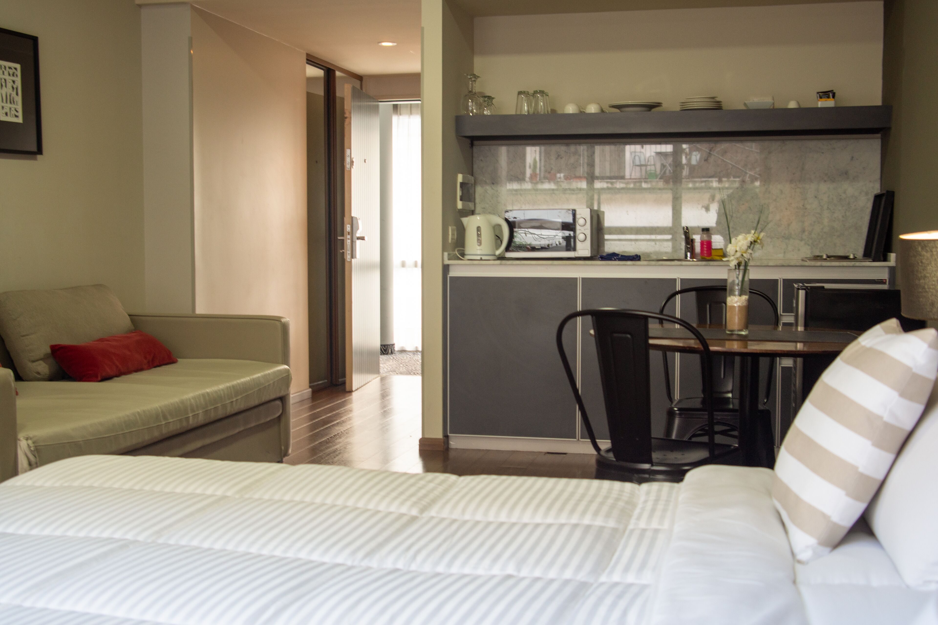 Ein kompaktes Hotelzimmer mit Bett, Schlafsofa, Esstisch mit Stühlen, einer Küchenzeile und Blick ins Freie.
