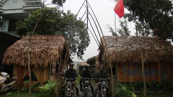 Three motorcyclists in front of thatched-roof huts with a sign reading "Hahaland".