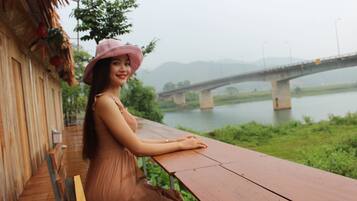 A person seated at a wooden table with a view of a bridge over a river.