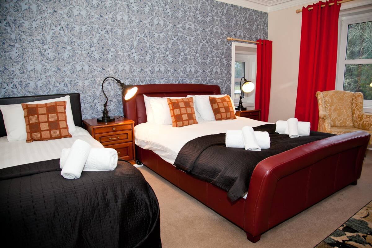 A hotel room with two beds, a red headboard, white linens, and a patterned wallpaper.
