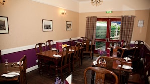 A restaurant with wooden tables and chairs, framed pictures on the walls, and a window with curtains. - Richmond House Hotel (Fort Augustus)