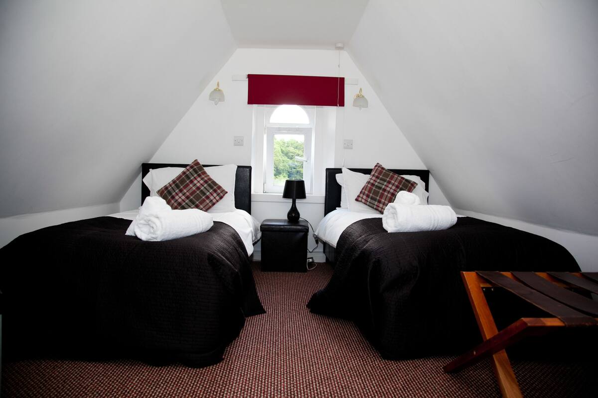 A room with two beds, a red curtain, a window, and a small table.