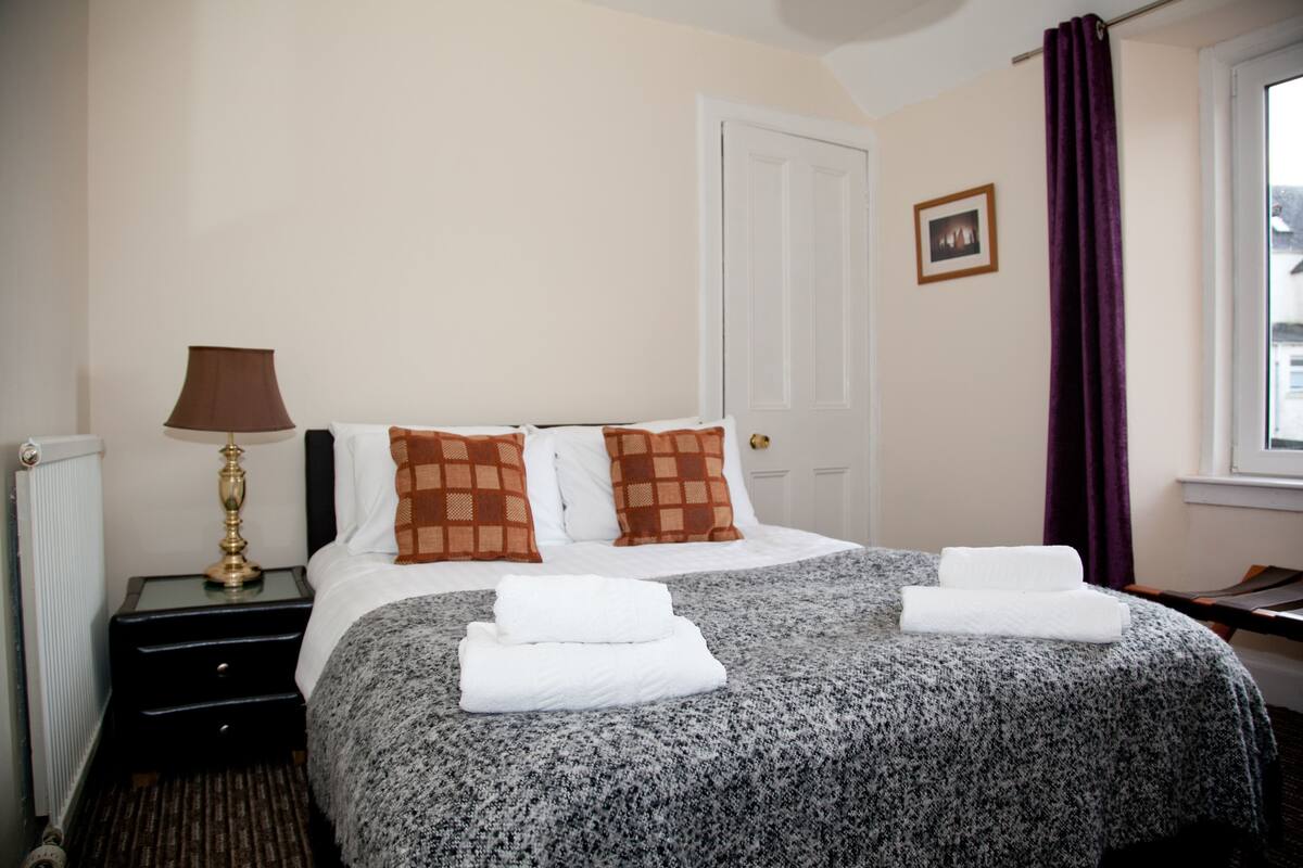 A neatly made bed with a patterned bedspread, two pillows, and folded towels.