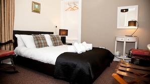 A hotel room with a bed, a desk, a chair, a lamp, and a mirror. - Richmond House Hotel (Fort Augustus)