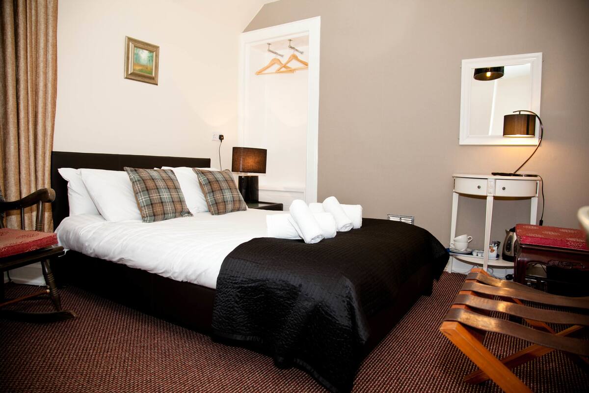 A hotel room with a bed, a desk, a chair, a lamp, and a mirror.