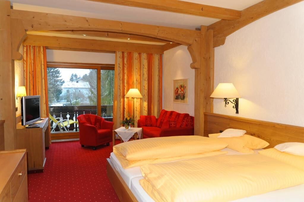 Ein Hotelzimmer mit einem großen Bett, einem roten Sofa, einem Fernseher und einem Balkon mit Blick auf Bäume.
