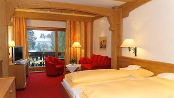 Ein Hotelzimmer mit einem großen Bett, einem roten Sofa, einem Fernseher und einem Balkon mit Blick auf Bäume.