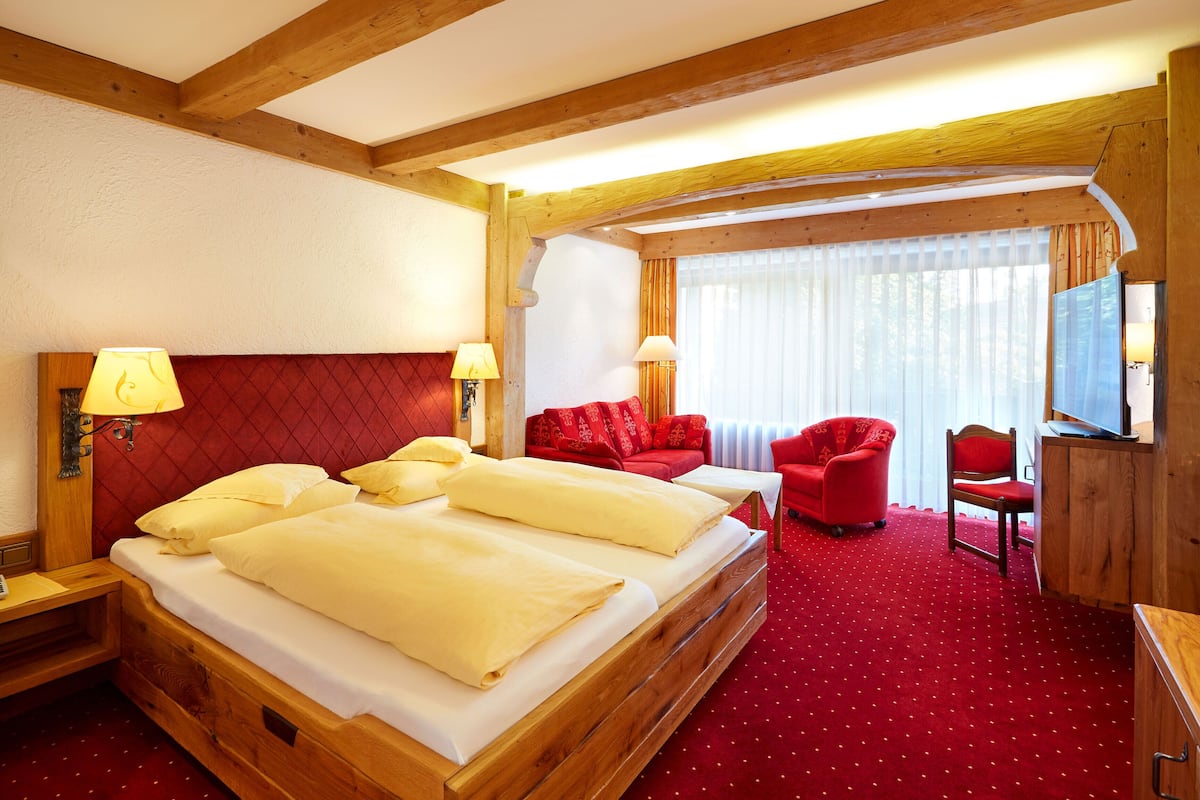 Une chambre d’hôtel avec un grand lit, deux lampes de chevet, un canapé rouge, un fauteuil rouge, un bureau en bois et un téléviseur.