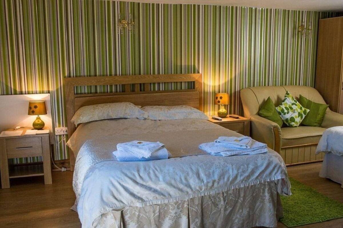 A bedroom with a large bed, two bedside tables with lamps, a chair with cushions, and a green-striped wall.