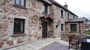 A stone building with a traditional design, featuring a stone facade, multiple windows with wooden frames, and a small outdoor seating area with a table and chairs. - Pentre Riding Stable and Accommodation (Swansea)