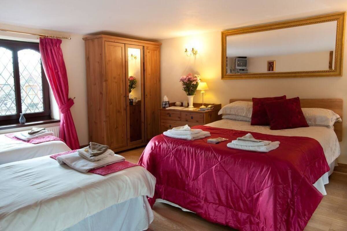A hotel room with two beds, a wooden wardrobe, a mirror, and a window with curtains.